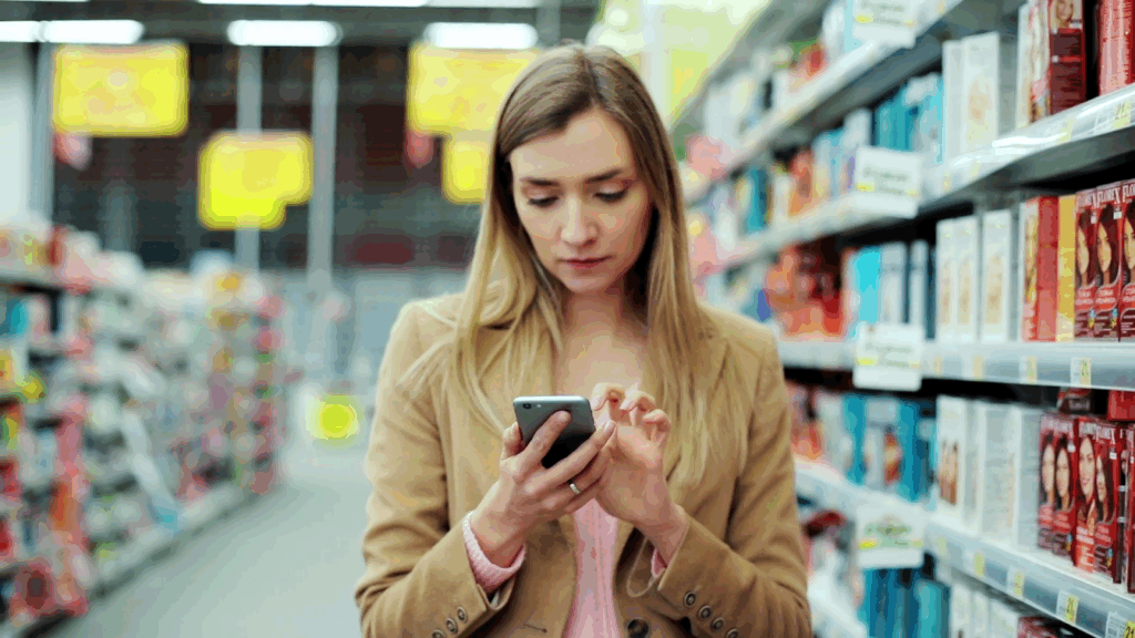 videoblocks-young-attractive-woman-use-phone-chooses-hair-dye-in-supermarket-smartphone-buyer-communication-store-cellphone-internet-holding-casual-everyday-hand-communicate-happy-message-1-1024x576 Varejo em Declínio: O Mistério Por Trás da Queda do Consumo Que Passa Despercebido